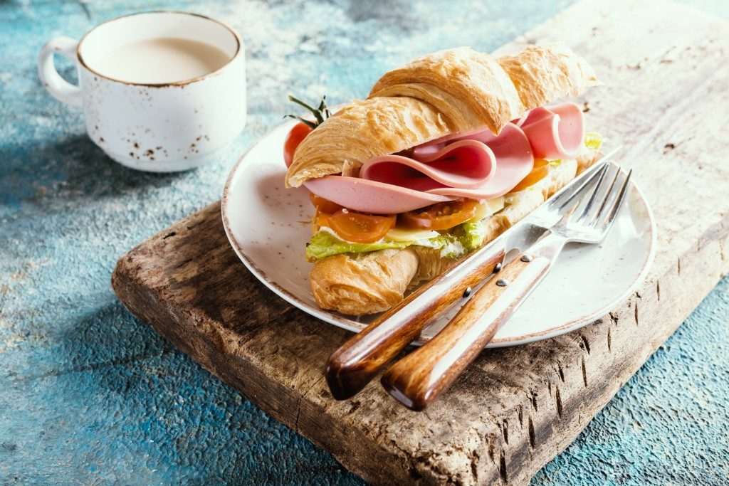 Fresh croissant sandwich with ham, cheese and salad leaf with coffee on blue table