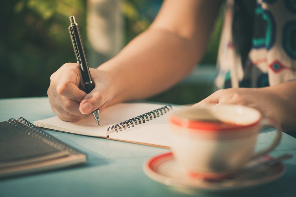 Woman hand writing journal on small notebook at outdoor area in cafe