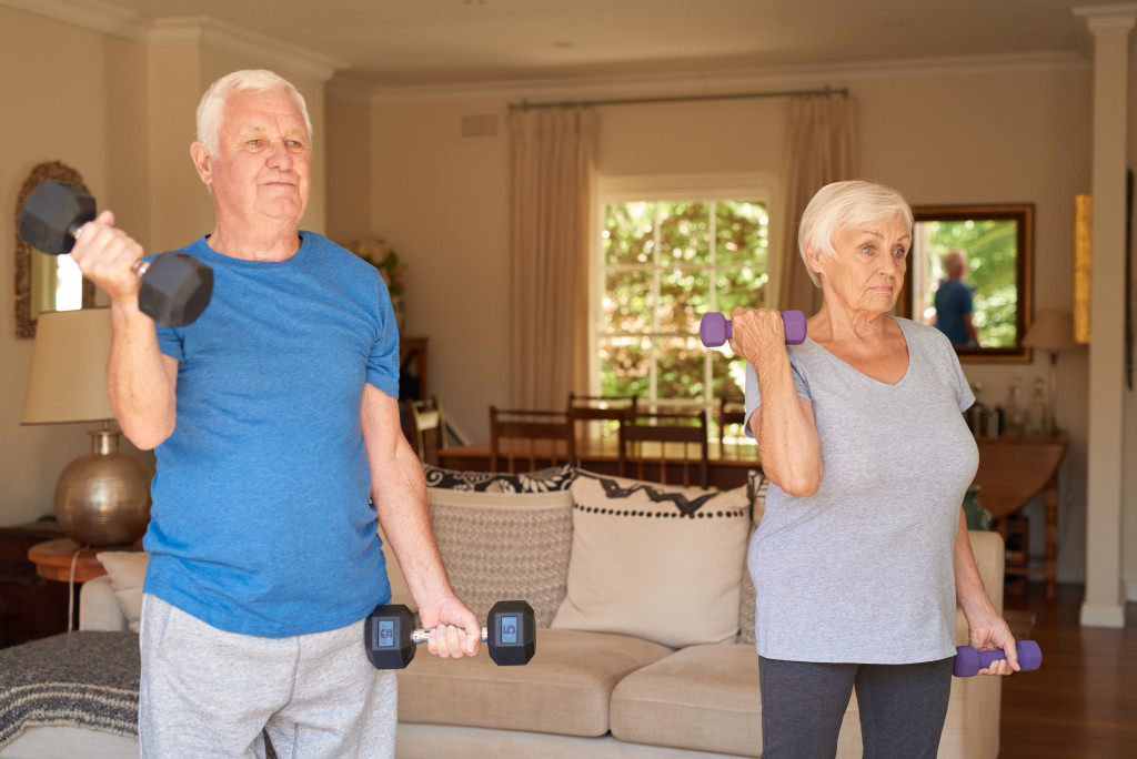 An elderly couple lifting dumbbells in their home living room