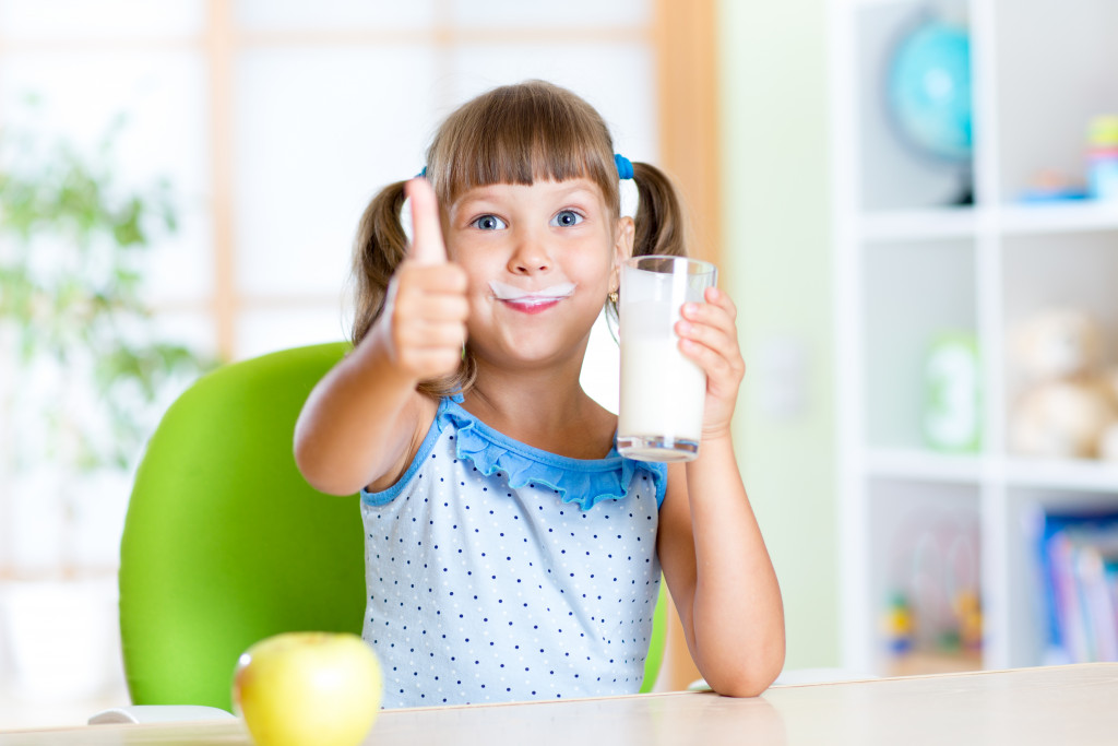 a little girl drinking a glass of milk with thumbs up