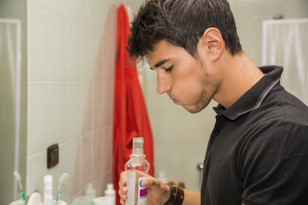 person rising their mouth using mouthwash in bathroom
