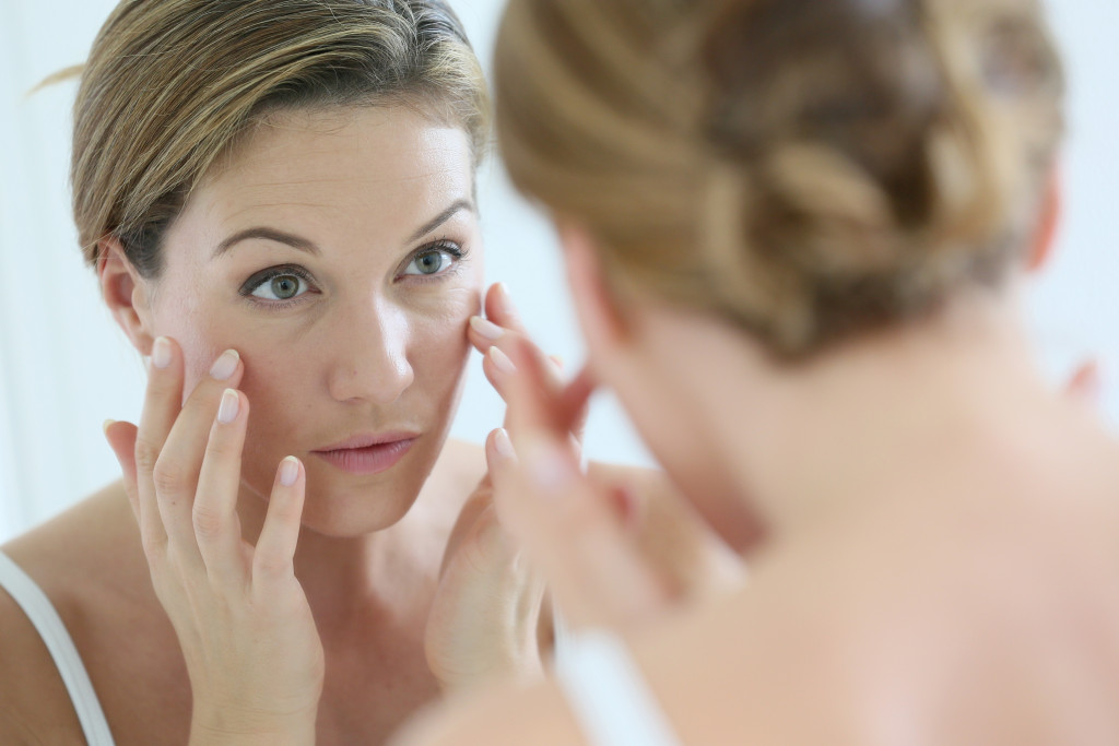 A woman applying facial cream on her face while looking at the mirror