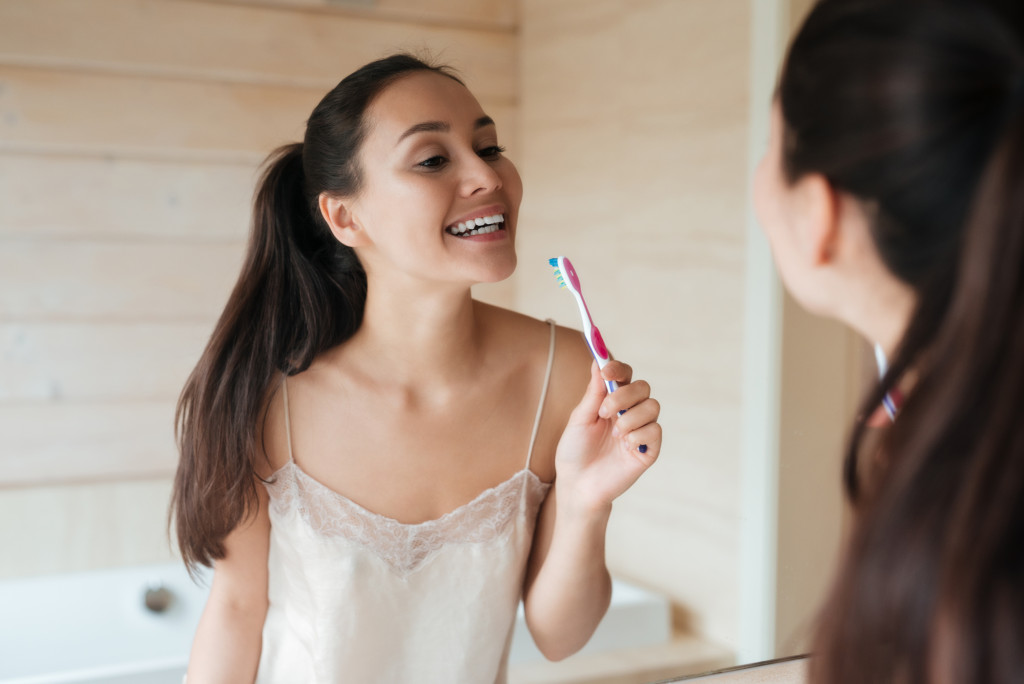young woman looking at the mirror and brushing her teeth