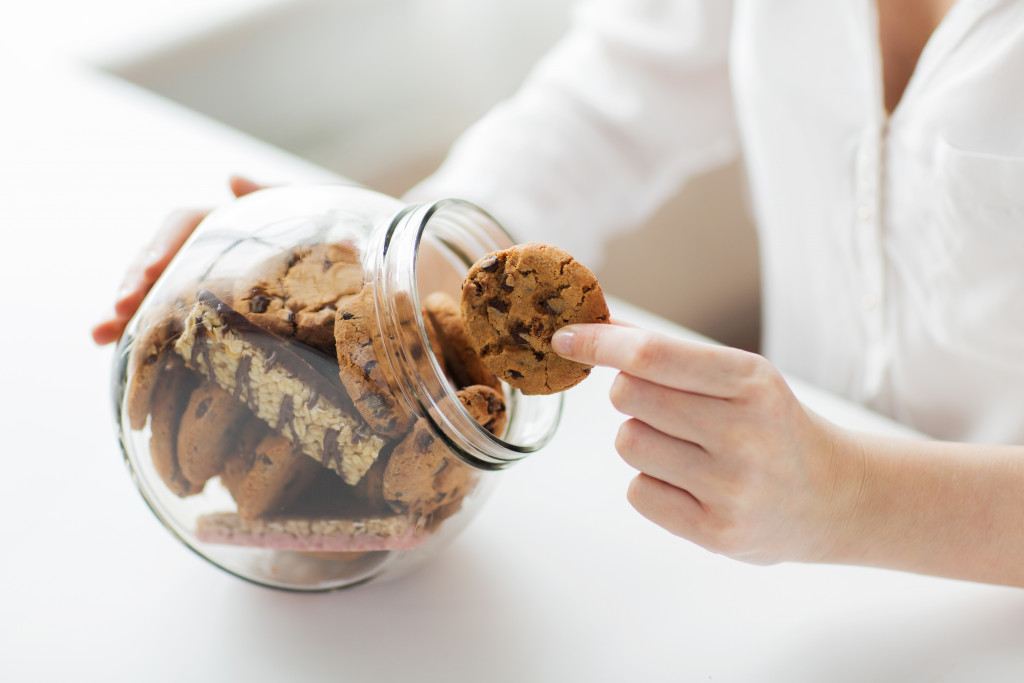 close up of hands with chocolate oatmeal cookies and muesli bars in glass jar