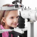 optometrist performing eye test on young girl in eyeglass store or clinic
