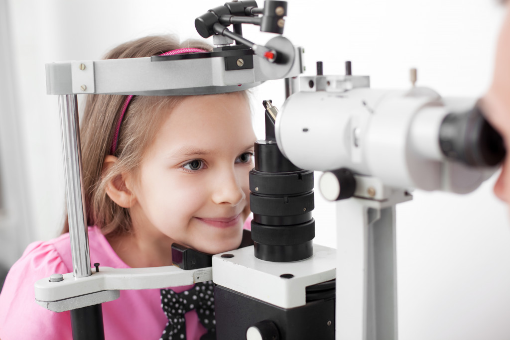optometrist performing eye test on young girl in eyeglass store or clinic